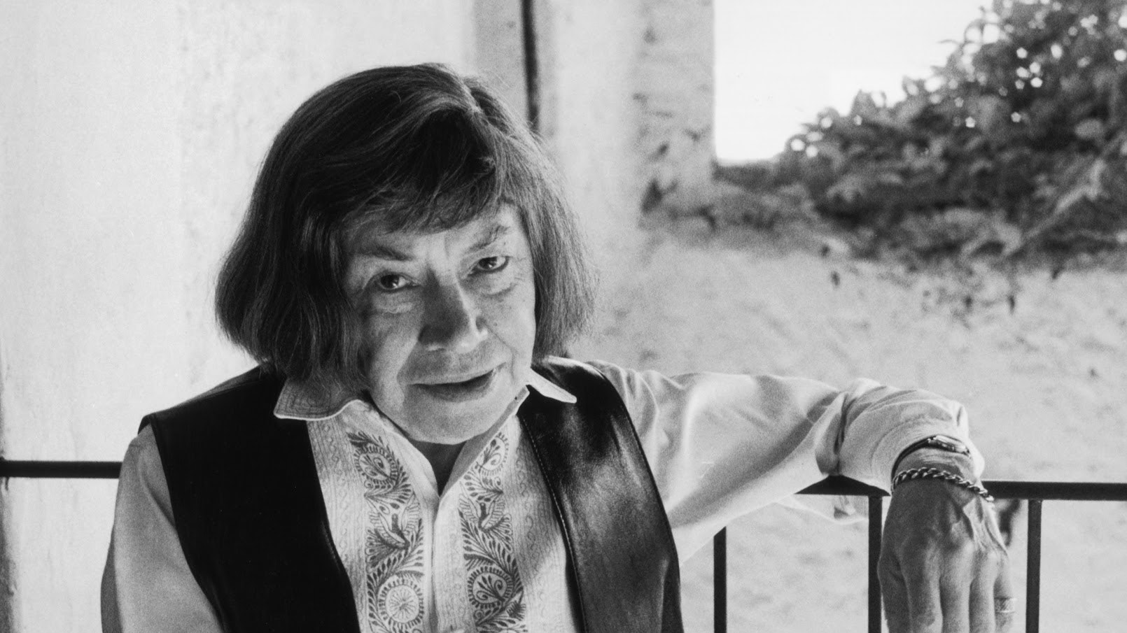 circa 1990:  A portrait of American writer Patricia Highsmith (1921 - 1995) leaning on a railing while sitting on a bench overlooking a courtyard. She is wearing a leather vest with tassels and an embroidered shirt.  (Photo by Horst Tappe/Hulton Archive/Getty Images)